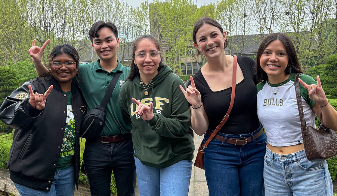Five people smile for the camera, making the USF Bulls hand sign.