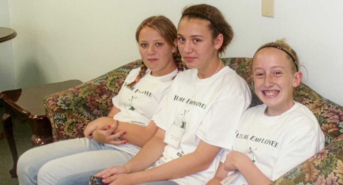 Three girls wearing "Future Employee" T-shirts seated on a couch.